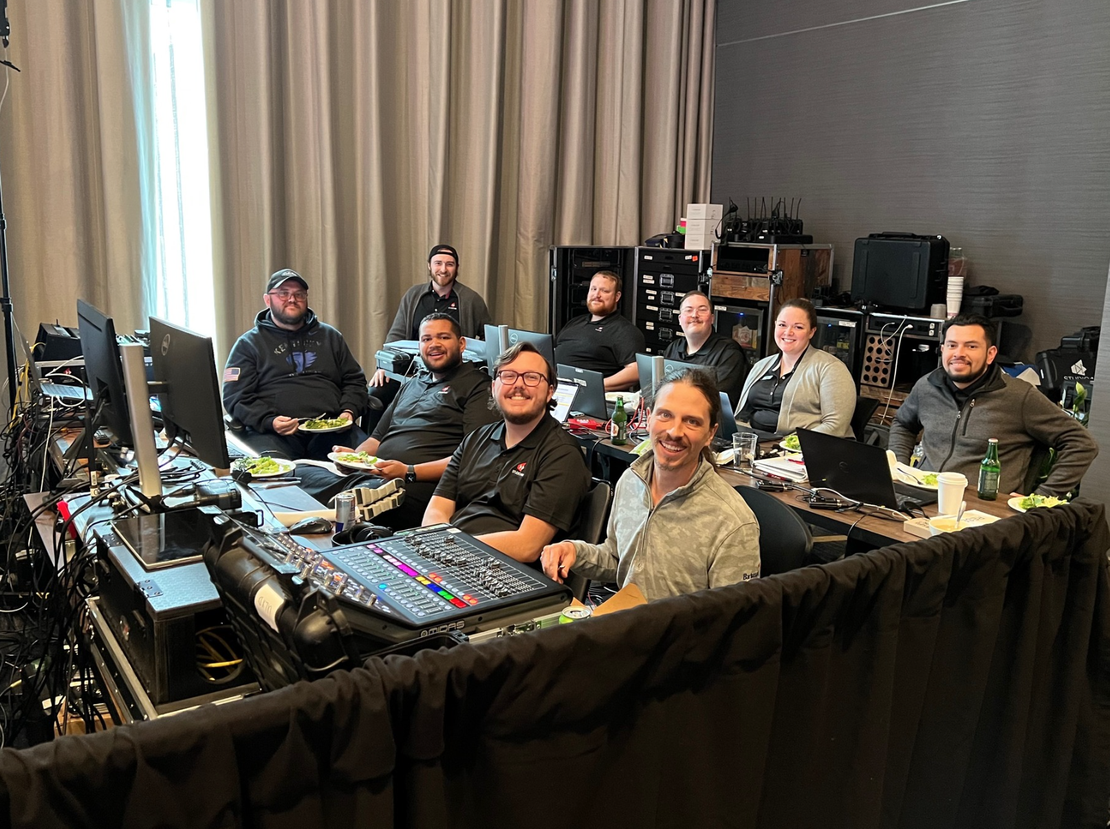 Studio46 team smiling at the camera while sitting at tables filled with various audio, visual equipment.